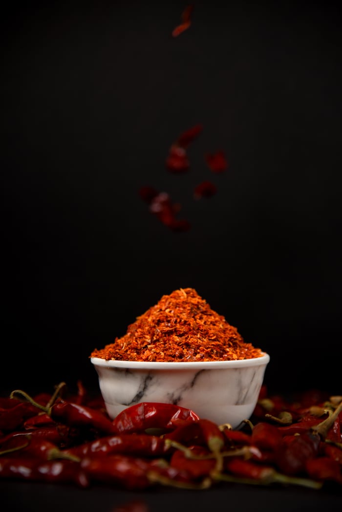 Red chili powder in a marble bowl with dried chilies on black background.
